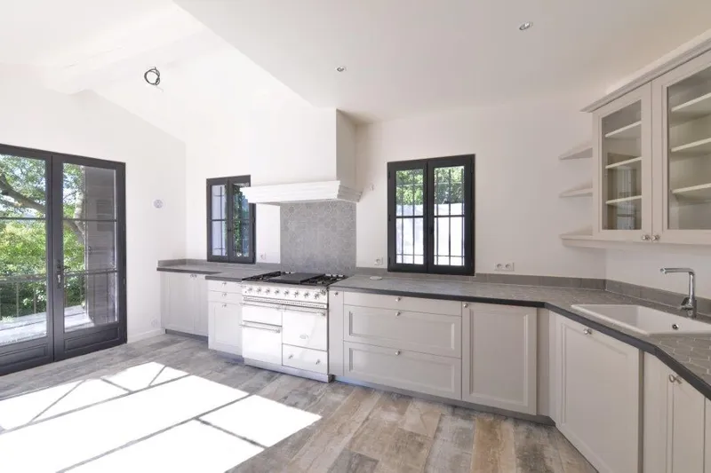 Cuisine blanche rénovée avec parquet et grandes fenêtres sur jardin