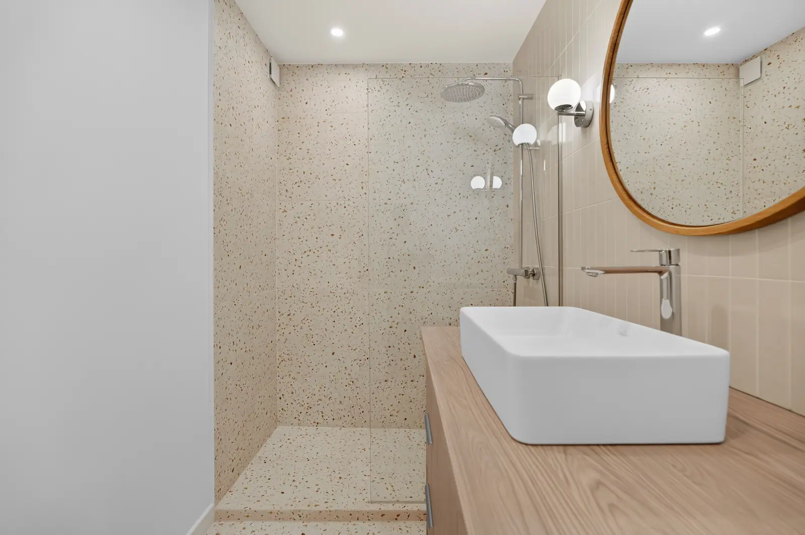 Salle de bains en terrazzo avec douche et vasque sur meuble bois