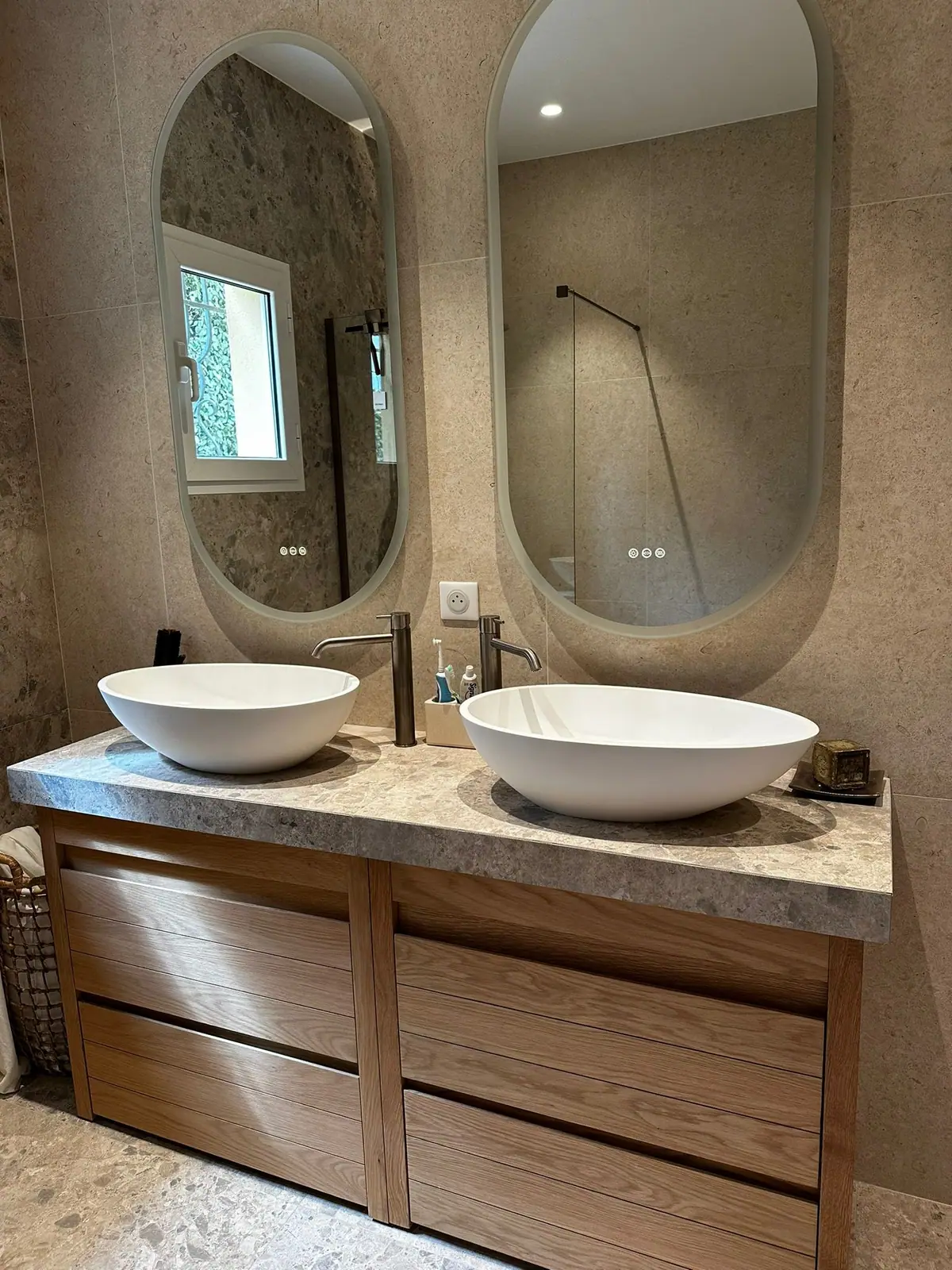 Double vasque sur meuble bois et miroirs ovales, salle de bains effet pierre
